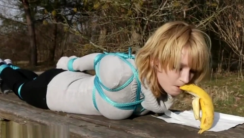 Cute girl eats banana while tied outside